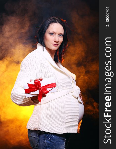 Young and beautiful pregnant woman on black background with smoke