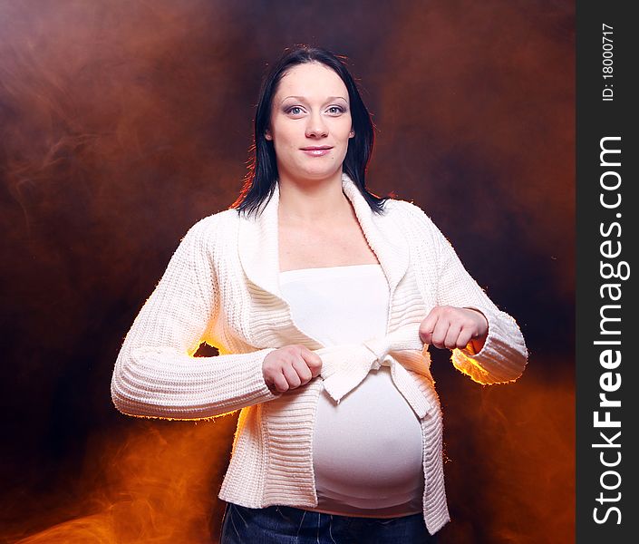 Young and beautiful pregnant woman on black background with smoke