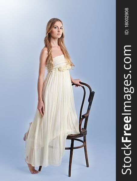 Young fashionable blond girl in long dress near the chair