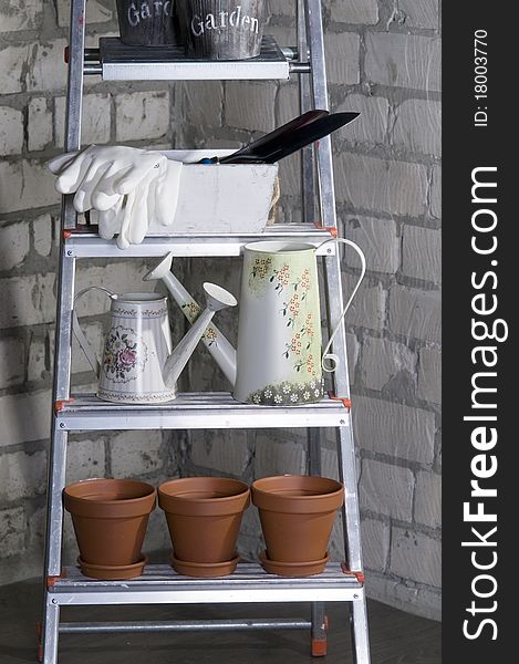 Gardening tools on a metal stepladder over grey brick wall.