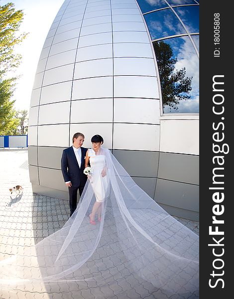 Bride and groom by the wall with long flying veil