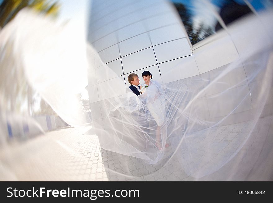 Bride and groom by the wall with long flying veil