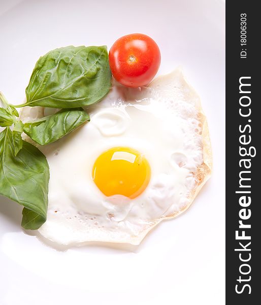 Fried egg served on a white plate with tomato and fresh herbs. Fried egg served on a white plate with tomato and fresh herbs