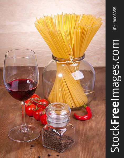 Composition of pasta, pepper, tomato and glass of red wine on the wooden table. Composition of pasta, pepper, tomato and glass of red wine on the wooden table