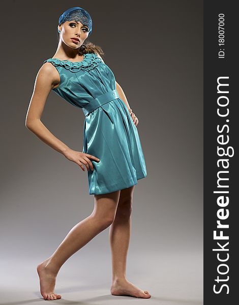 Beautiful blond model in blue lucid dress posing on grey background