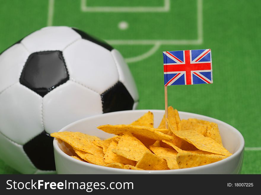 Soccer ball with crispy snacks in a bowl on green background