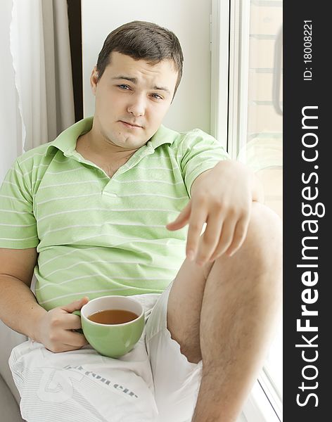 Young man drinking tea on a windowsill