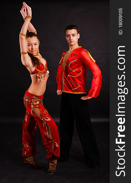 A beautiful young pair in good-looking suits dances on a dark background. A beautiful young pair in good-looking suits dances on a dark background