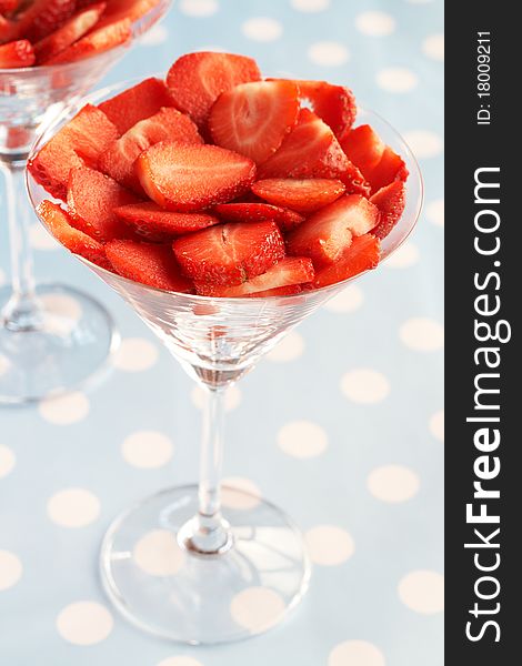 Sliced fresh strawberries in martini glasses on blue polka dot background. Sliced fresh strawberries in martini glasses on blue polka dot background