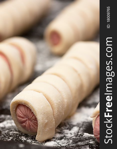 Raw sausage rolls in pastry on a baking tray