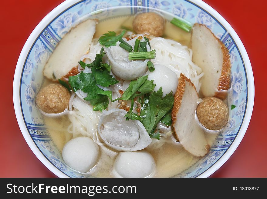 Wide rice noodle soup with vegetables and meat ball fish ball on red blackground