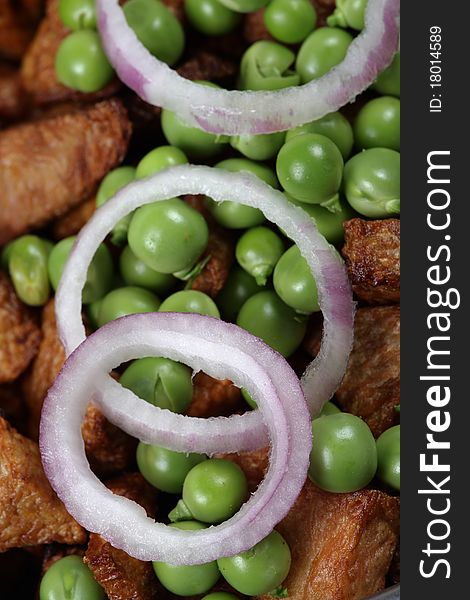 Closeup shot of onion rings and green peas on fried potatoes.