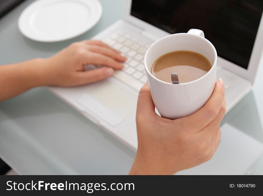 A woman taking a coffee break holding a cup of coffee while working. A woman taking a coffee break holding a cup of coffee while working