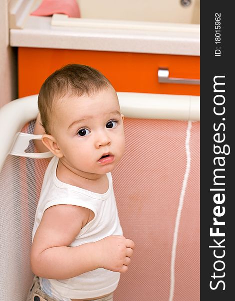 Cute caucasian baby in manege, kitchen housework