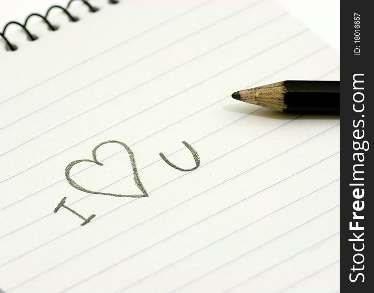 Pencil and small notebook with a love valentine message saying i love you, lying on a white surface