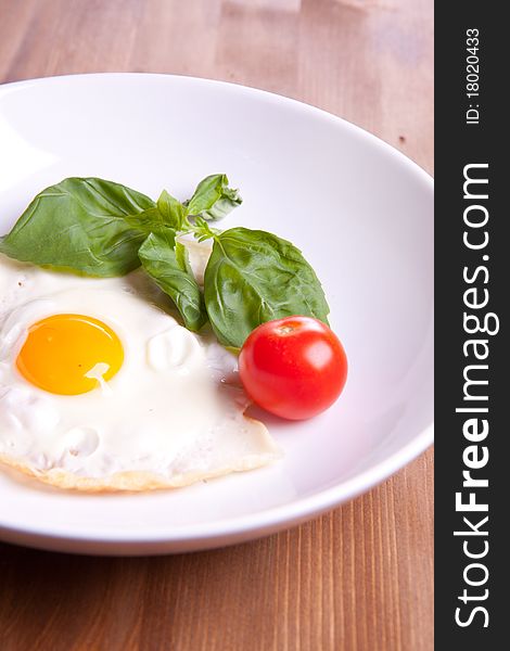 Fried egg served on a white plate with tomato and fresh herbs. Fried egg served on a white plate with tomato and fresh herbs