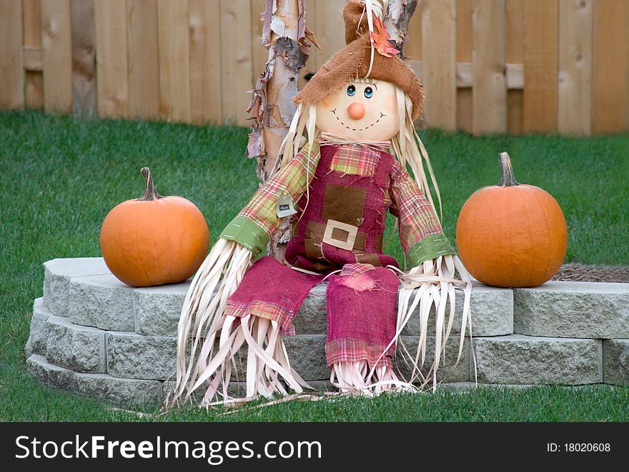Scarecrow sitting on a brick ledge in the Autumn with two pumpkins. Scarecrow sitting on a brick ledge in the Autumn with two pumpkins.