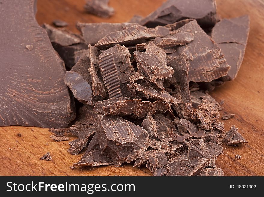 Bitter chocolate in pieces on a brown background in a plate.