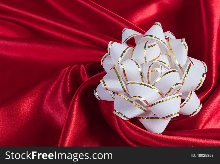 White gift bow on an elegance red silk background. White gift bow on an elegance red silk background