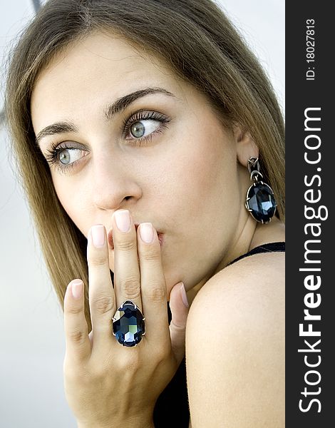 Portrait of elegantly beautiful young woman covers her mouth with his hand. Girl beautiful jewelry with large blue stones