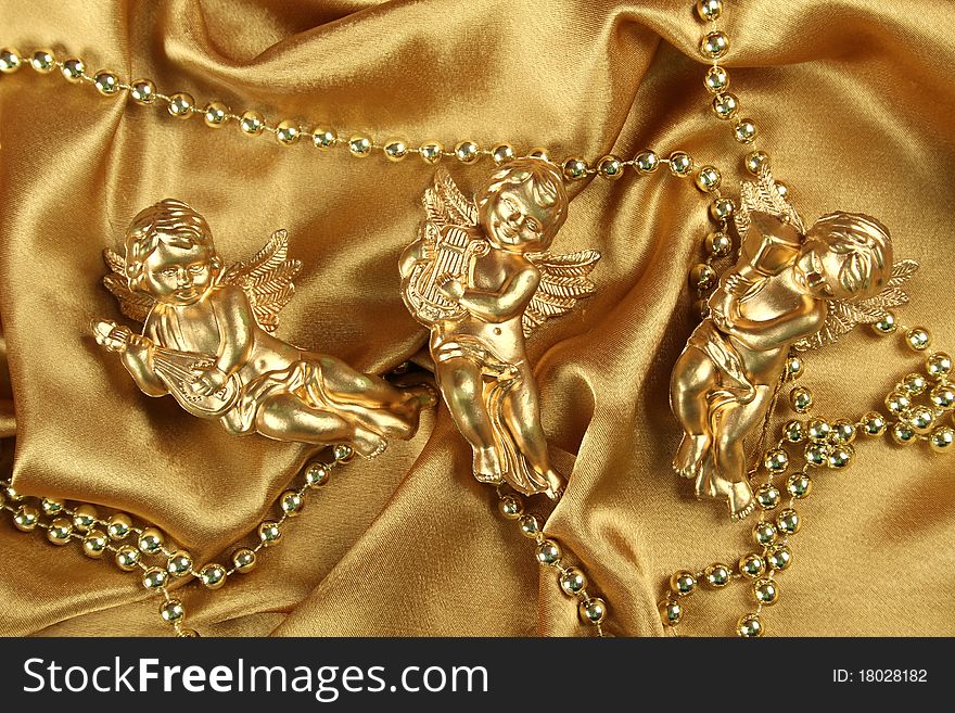 Three small gold angel with a harp lying on the golden cloth beside ornaments. Background