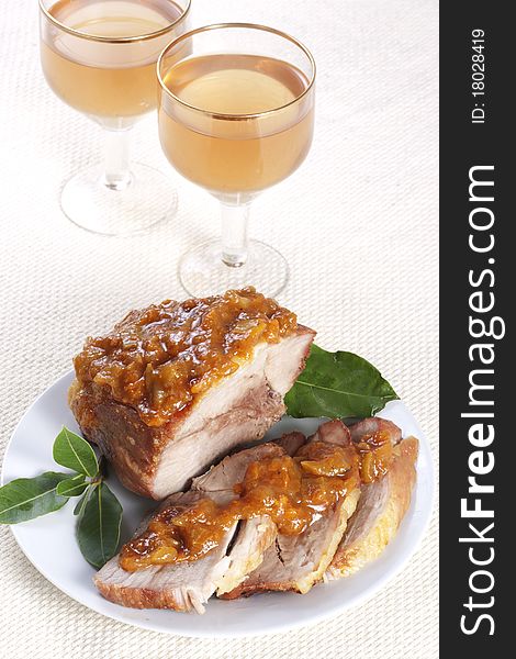 Roasted pork with apricot sauce on a plate and two glasses of wine