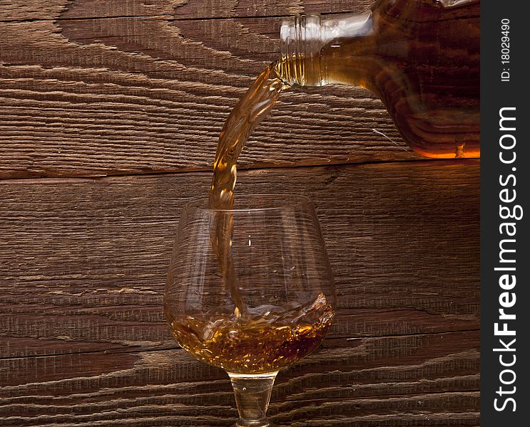 Cognac pour from a bottle in a glass on wood background