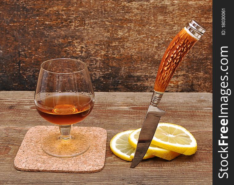 Classic cognac with lemon and knife on wood background