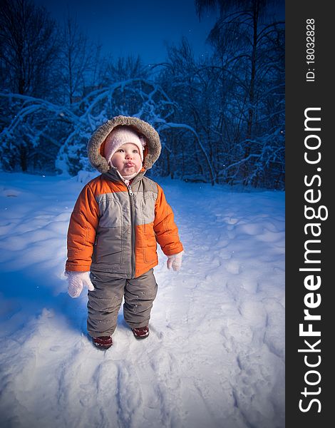 Adorable baby walking in evening park. Stay on snow road look up