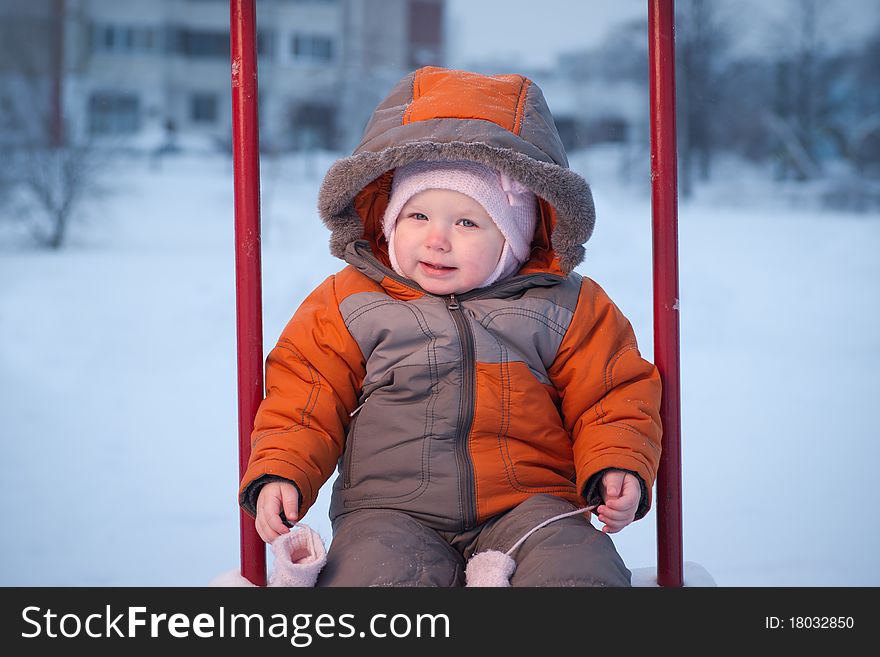 Cute baby sit on swing in winter evening. Taking out the mittens. Cute baby sit on swing in winter evening. Taking out the mittens