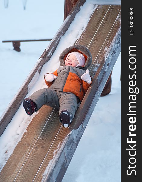 Cute baby sliding down the slides for children in winter