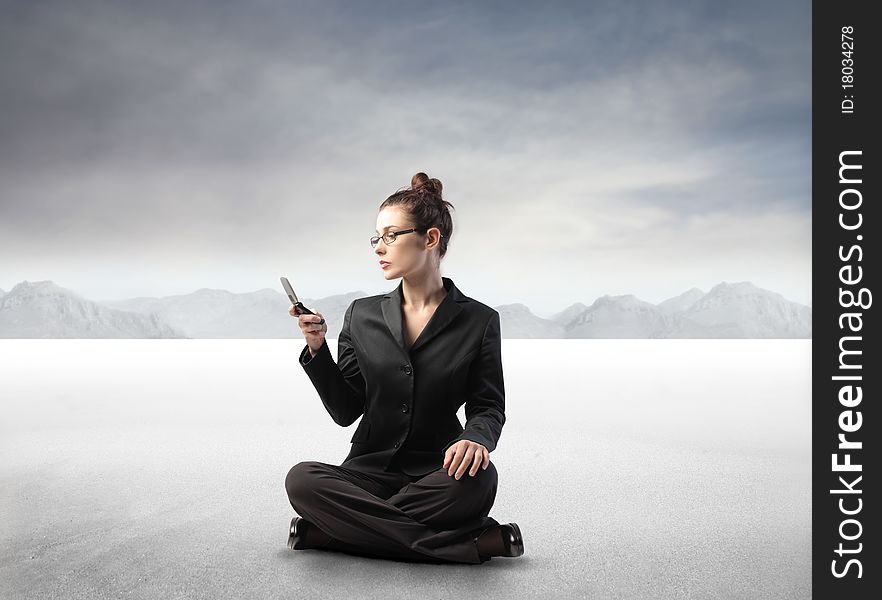 Businesswoman sitting in a desert and using a mobile phone. Businesswoman sitting in a desert and using a mobile phone