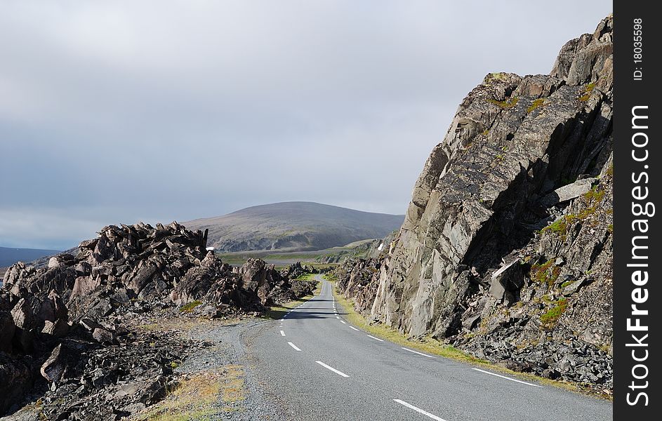 Asphalt road is meandering between among rocks of north Norwegian coast. This is the road to Hamningberg. Highway is photographed with diminishing perspective. Asphalt road is meandering between among rocks of north Norwegian coast. This is the road to Hamningberg. Highway is photographed with diminishing perspective.
