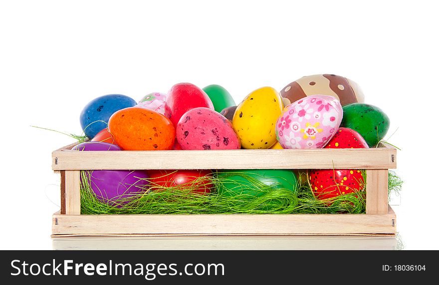 A cheerful wooden box with varied sorts of painted plastic and candy easter eggs isolated over white. A cheerful wooden box with varied sorts of painted plastic and candy easter eggs isolated over white