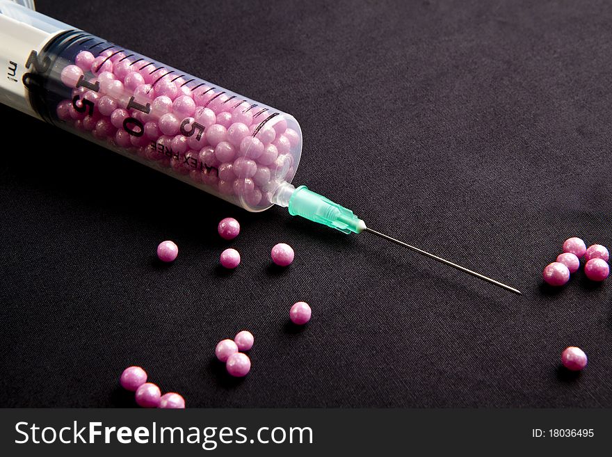 Syringe filled with pink candy on a black background