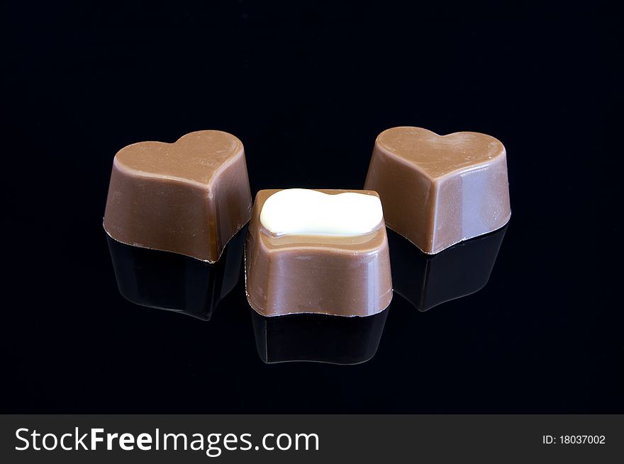 Three chocolates on a black background with reflection. Close-up. Three chocolates on a black background with reflection. Close-up