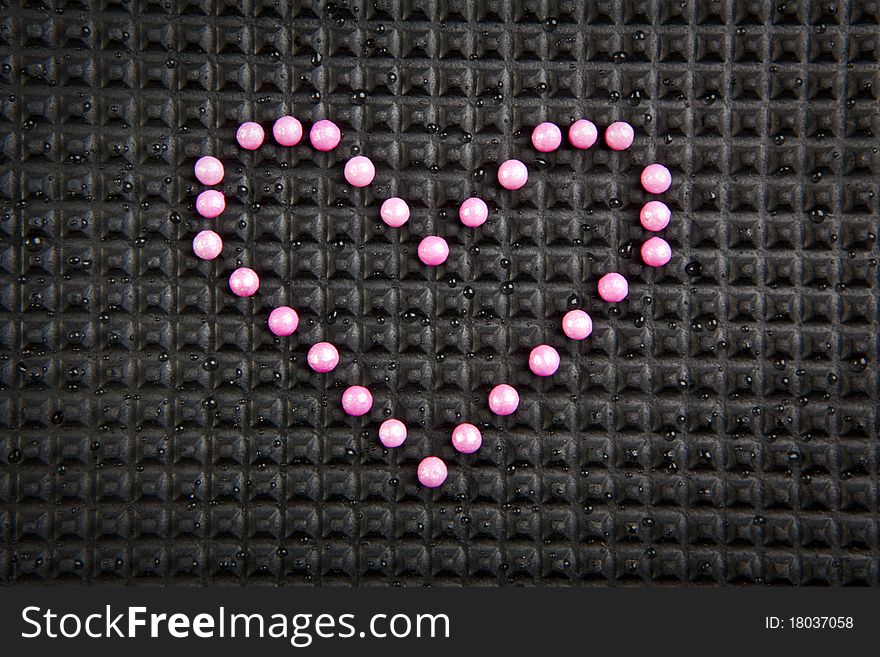 Heart shape made with candy on rubber black background