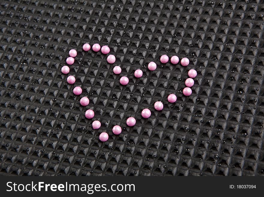 Heart shape made with candy on rubber black background