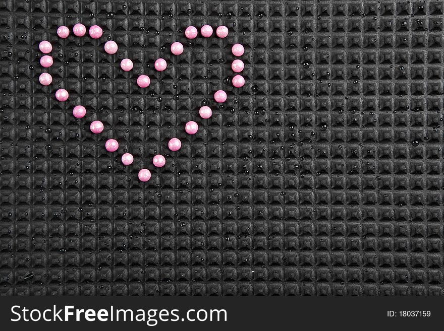 Heart shape made with candy on rubber black background