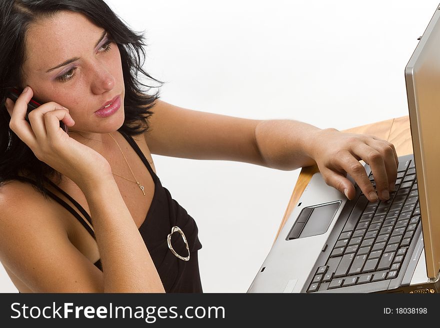 Young smiling brunette business woman typing on a laptop and talking on a cellphone. Young smiling brunette business woman typing on a laptop and talking on a cellphone