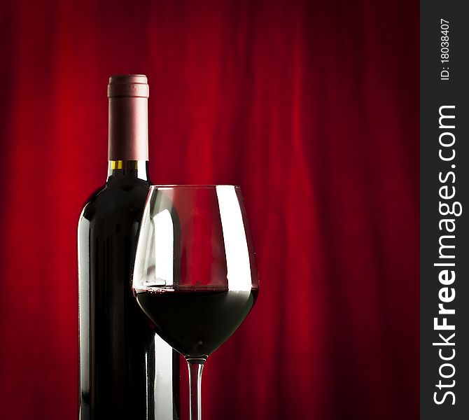 A glass of red wine and a bottle on red background