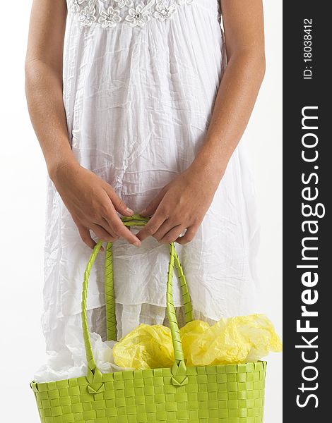 Cropped image of the body of a young tanned healthy woman in a white summer cotton dress holding a green woven shopping bag. Cropped image of the body of a young tanned healthy woman in a white summer cotton dress holding a green woven shopping bag