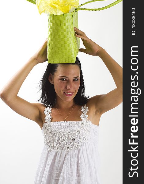 Young tanned healthy woman in a white summer cotton dress and yellow sandals balancing a green woven shopping bag on her head. Young tanned healthy woman in a white summer cotton dress and yellow sandals balancing a green woven shopping bag on her head