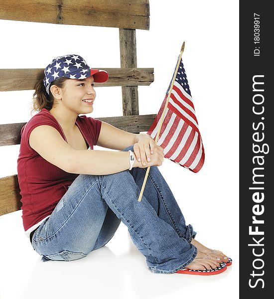 An attractive young teen holding an American flag and wearing a stars and stripes hat sitting against a rustic rail fence. Isolated on white. An attractive young teen holding an American flag and wearing a stars and stripes hat sitting against a rustic rail fence. Isolated on white.