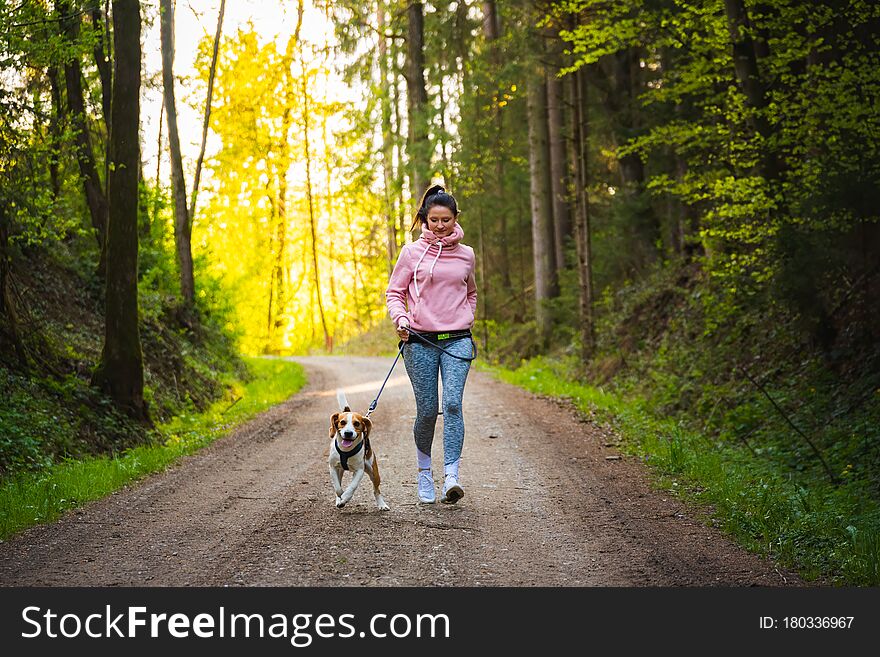 Young woman and dog running together on country in forest. Cheerful female exercising outdoor with her pet. Active people concept