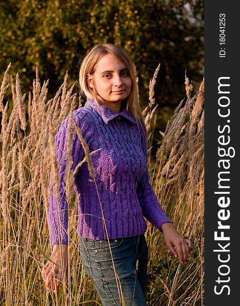 A girl in a lilac pullover and jeans in grass. A girl in a lilac pullover and jeans in grass