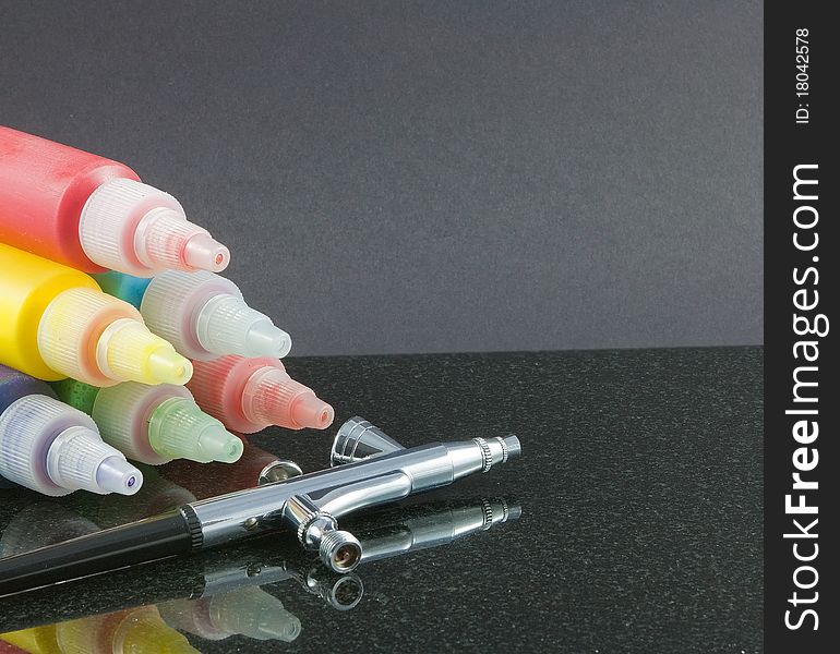 A pyramid of colourful paints and a silver airbrush on a dark background. A pyramid of colourful paints and a silver airbrush on a dark background