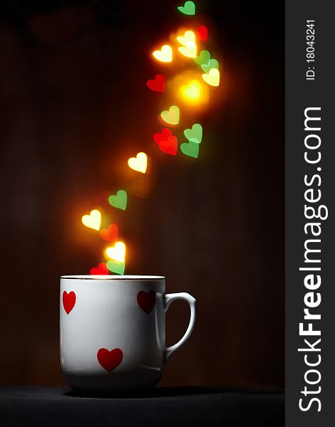 Mug emits steam of glowing hearts on dark background with copy space. Mug emits steam of glowing hearts on dark background with copy space