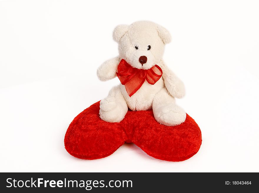 White teddy bear sitting on a heart shaped pillow isolated on white background