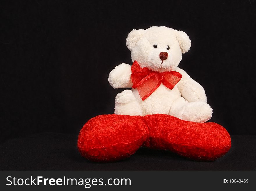 White teddy bear sitting on a heart shaped pillow isolated on black background